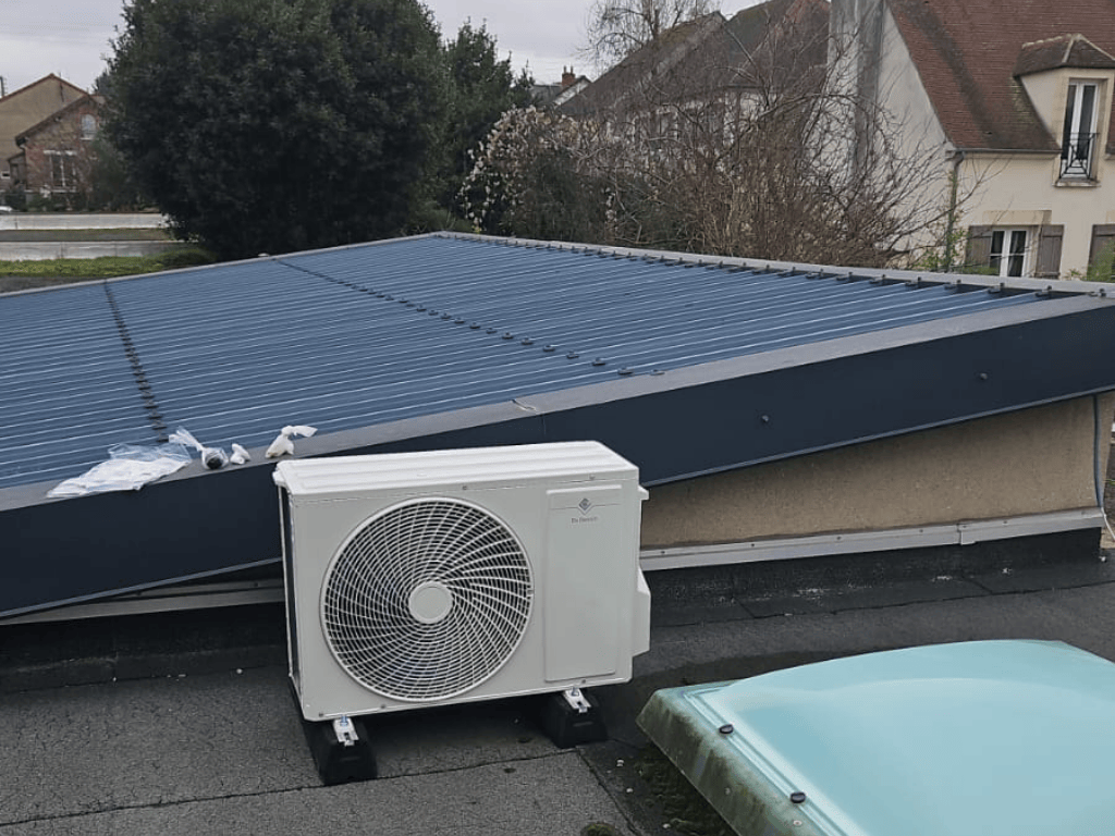 Unité extérieure de pompe à chaleur installée sur un toit terrasse à proximité d’une toiture résidentielle.